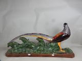 a figurine of a pheasant sitting on a green plant