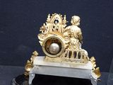 a gold clock on a marble stand with a glass vase