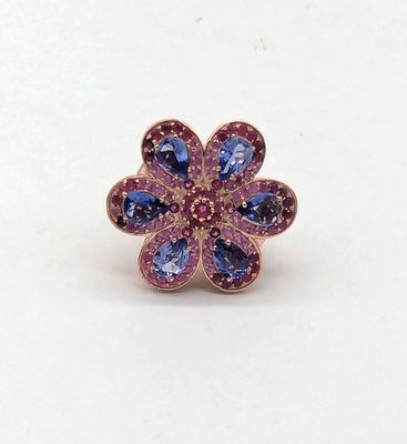 un gros plan d'une bague ornée d'une fleur violette et bleue sur un fond blanc