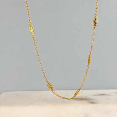 un collier à chaîne en or orné d'une breloque en forme de feuille posé sur une dalle de marbre