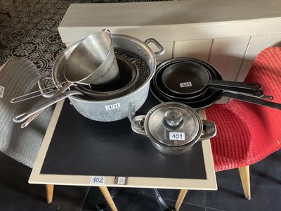 Plusieurs casseroles et poêles sont posées sur une table, accompagnées d'une étiquette de prix