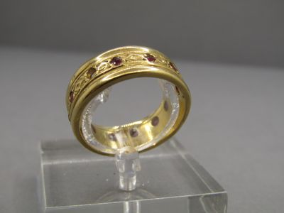 une bague en or sertie de pierres rouges, posée sur un socle transparent