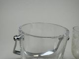 a glass ice bucket with a handle next to a glass of water