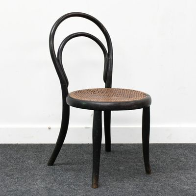 une image représentant une chaise noire avec une assise en osier, posée sur un sol recouvert de moquette