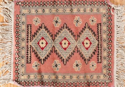 un vieux tapis à franges posé sur un parquet, près d'un mur