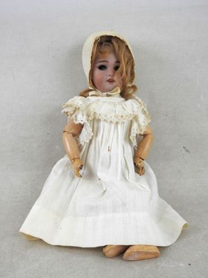 une poupée assise par terre, vêtue d'une robe blanche et d'un bonnet