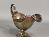 an antique silver sauce boat with a spoon on a stand