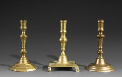 three brass candlesticks on a stand against a gray background