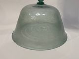 une cloche en verre avec un haut vert posée sur une surface blanche