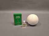 a golf ball next to a small bottle of perfume