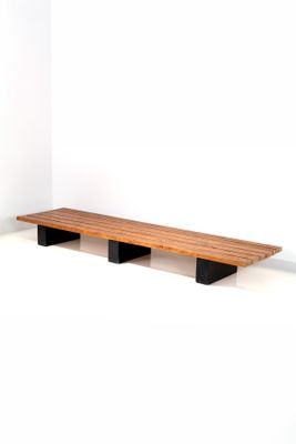 a wooden bench with two black legs in a white room