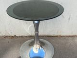 une table en verre avec un plateau noir posée sur un sol en béton