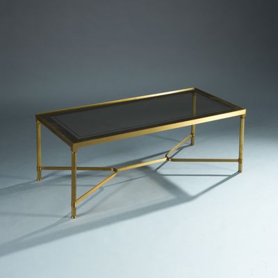 une table basse dorée avec un plateau en verre et des pieds en métal