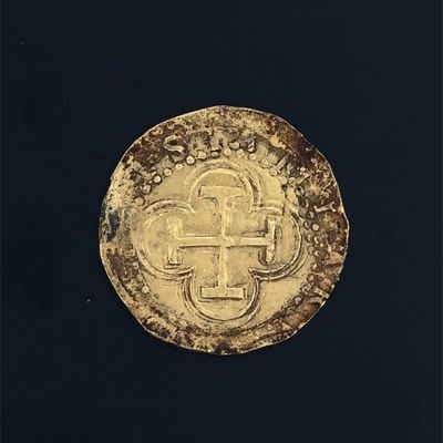 an old gold coin with a cross on it on a black surface