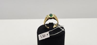 une bague en or sertie d'une pierre verte repose sur un présentoir à bagues noir