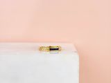 une bague en or ornée de deux pierres noires, posée sur un bloc de marbre blanc