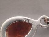 a close up of a silver pendant with a red stone