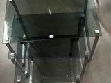 une table en verre avec un piètement en métal et une étagère en verre
