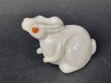 a small white rabbit figurine with an orange eye