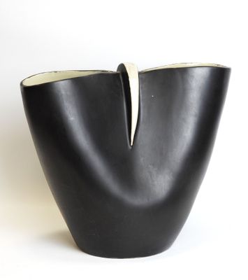 a black vase with a white handle sitting on a white surface