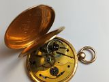 a gold pocket watch with a key on a white surface