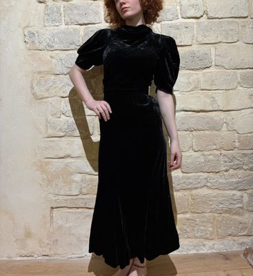 a woman standing in front of a brick wall wearing a black dress