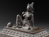 bronze statue of a woman sitting on a platform with a skull in her hand