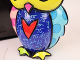 brightly colored owl figurine sitting on top of a desk next to a laptop computer