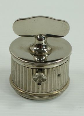 une petite boîte argentée avec un couvercle, posée sur une surface blanche