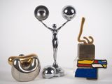 une statue en argent représentant un homme tenant une balle et une paire de ciseaux