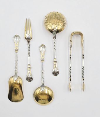 cinq cuillères et fourchettes en argent et en or, ainsi qu'un repose-cuillère, posés sur une surface blanche