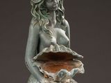 statue of a mermaid sitting on a rock with a shell in her hand