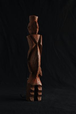 une sculpture en bois représentant une personne debout devant un fond noir