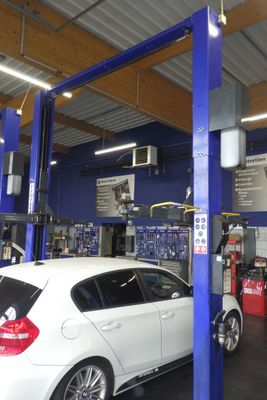 une voiture blanche garée dans un garage équipé d'un pont élévateur bleu