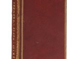 un vieux livre rouge avec des bordures dorées posé sur une surface blanche