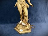 gold statue of a woman holding a lamp on top of a blue background