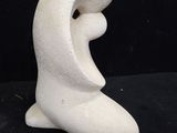 a white sculpture of a woman sitting on a black surface