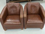 une paire de fauteuils club en cuir marron avec des pieds en bois, dans un magasin