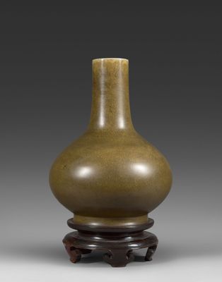 un vase brun posé sur un support en bois sur une surface grise
