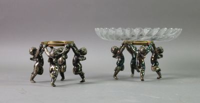 two silver figurines that are holding a bowl on their heads