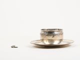 a silver cup and saucer sitting on a saucer