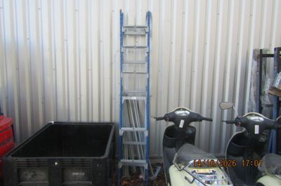 Plusieurs scooters sont garés devant un bâtiment métallique devant lequel se trouve une échelle.