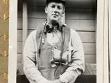 a black and white photo of a man in overalls and a hat