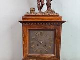 une horloge en bois surmontée d'une statue d'homme