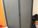 une armoire métallique dans un coin de la pièce, avec des cartons et une serpillière posés par terre
