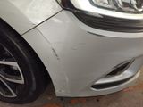the front end of a white car with a dent on it ' s bumper