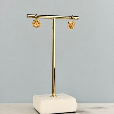 a pair of gold earrings sitting on top of a marble stand