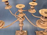 two antique brass candelabs with candles on stands on a blue background