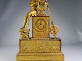 a gold clock with a woman sitting on top of it