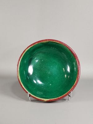 bol en céramique vert et rouge posé sur un socle, sur fond blanc